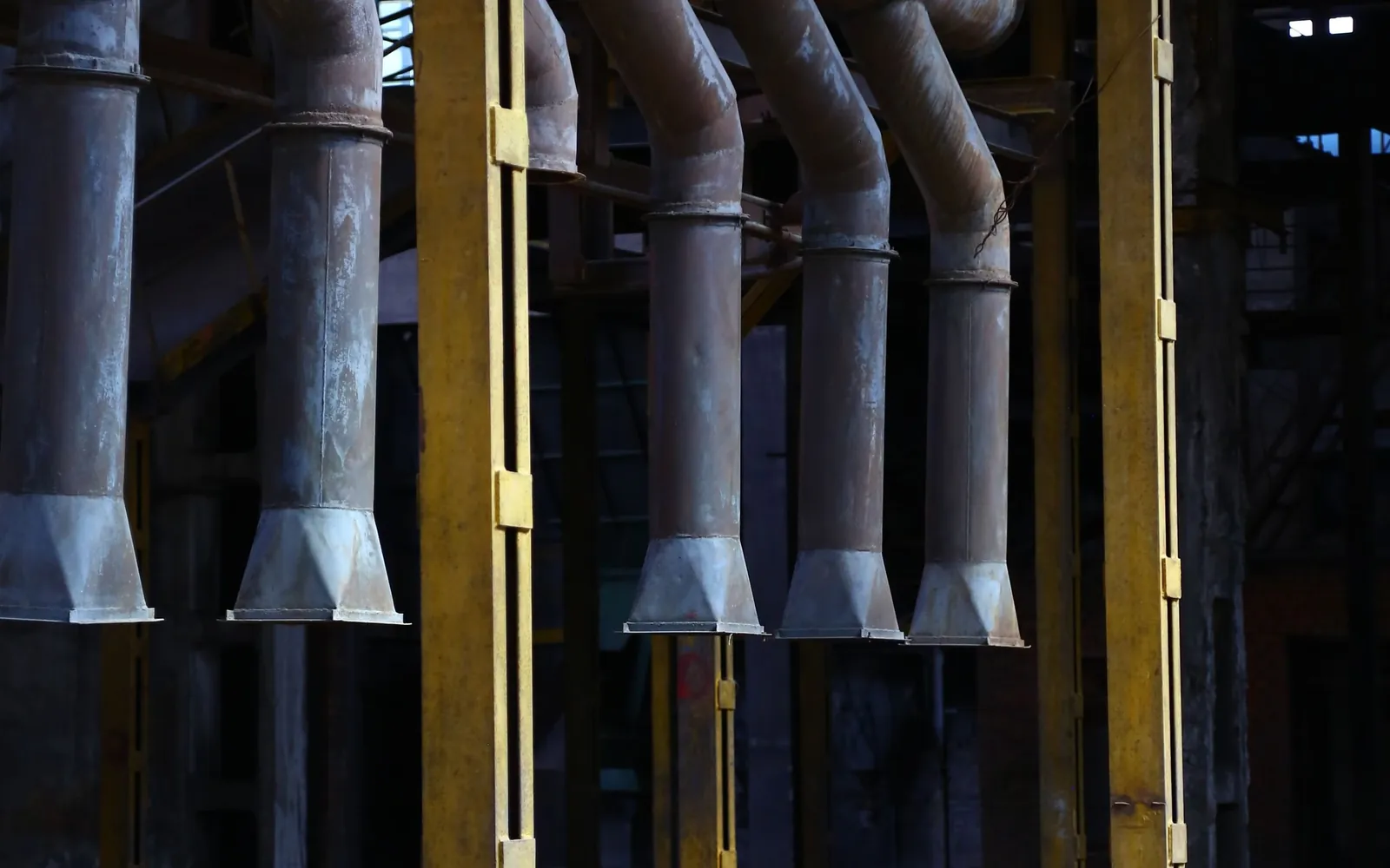 Industrial plant interior with rows of steel pipes and heavy machinery.