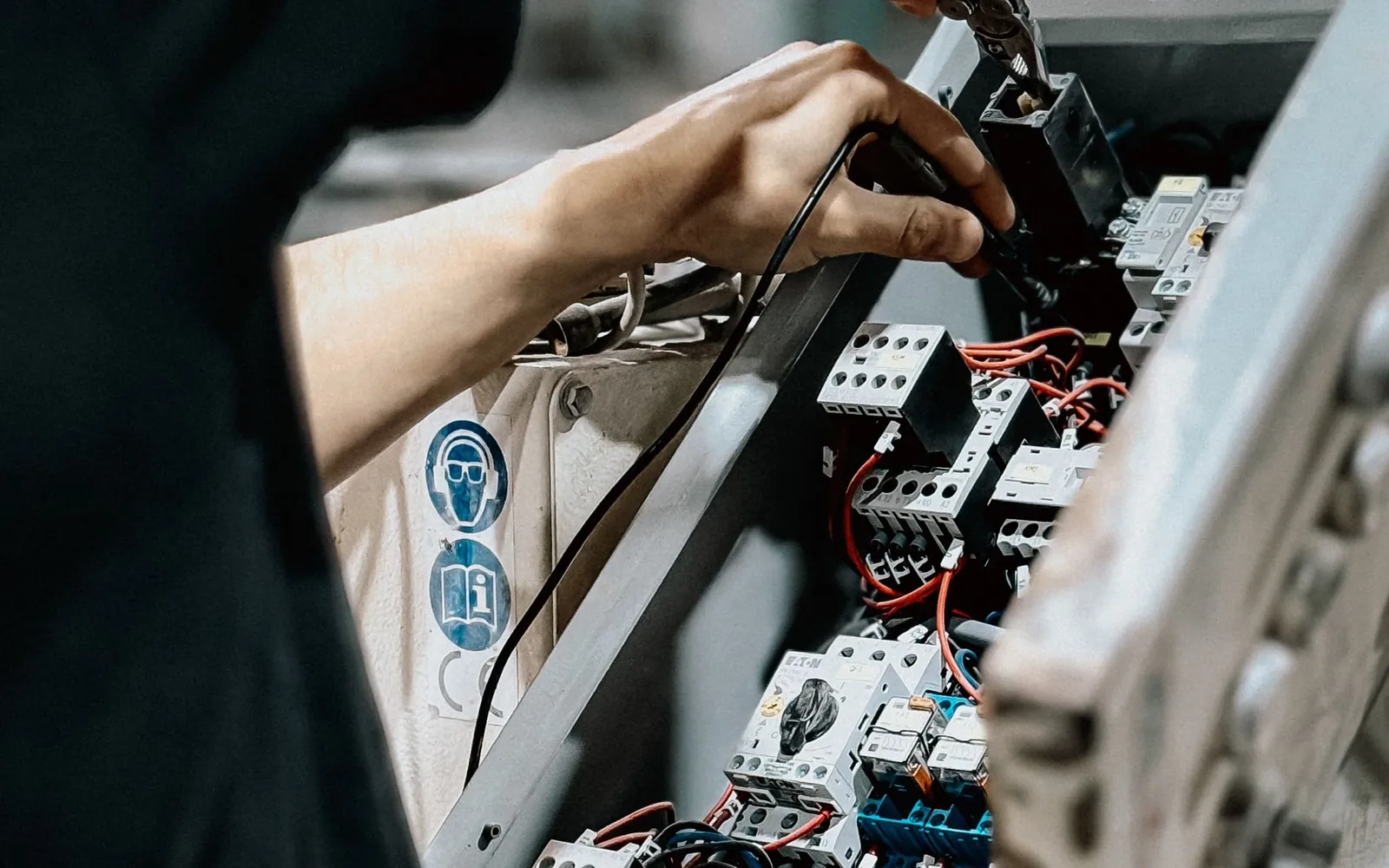 Technician adjusting wires inside an open electrical control panel.