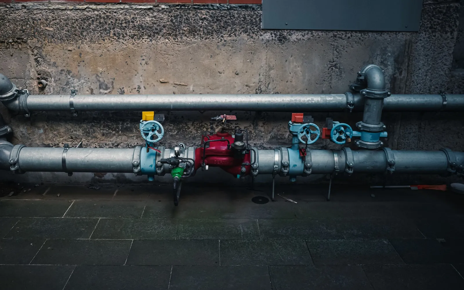 Industrial pipework with red, blue, and yellow hand valves.