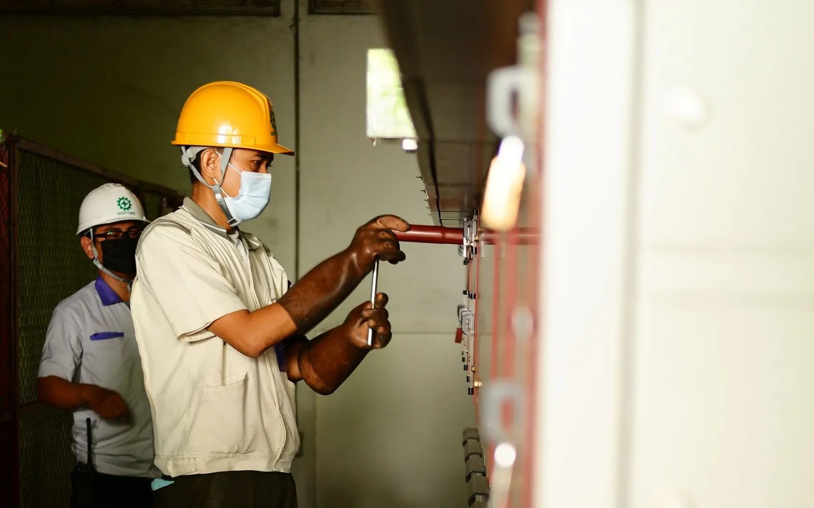 Two electricians working beside industrial electrical control panels.